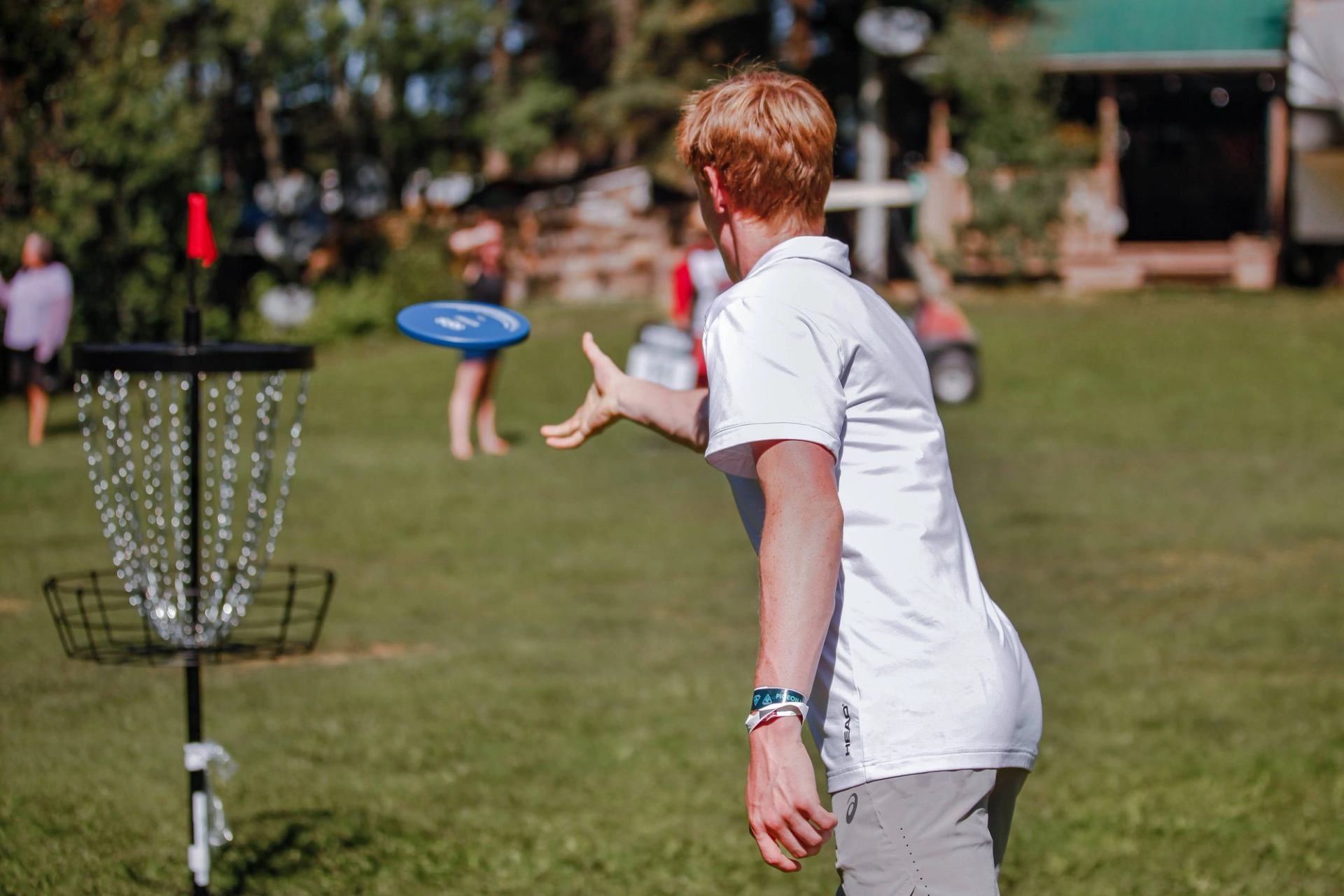 A person tossing a disc toward a disc golf basket on a grassy field during an outdoor event.