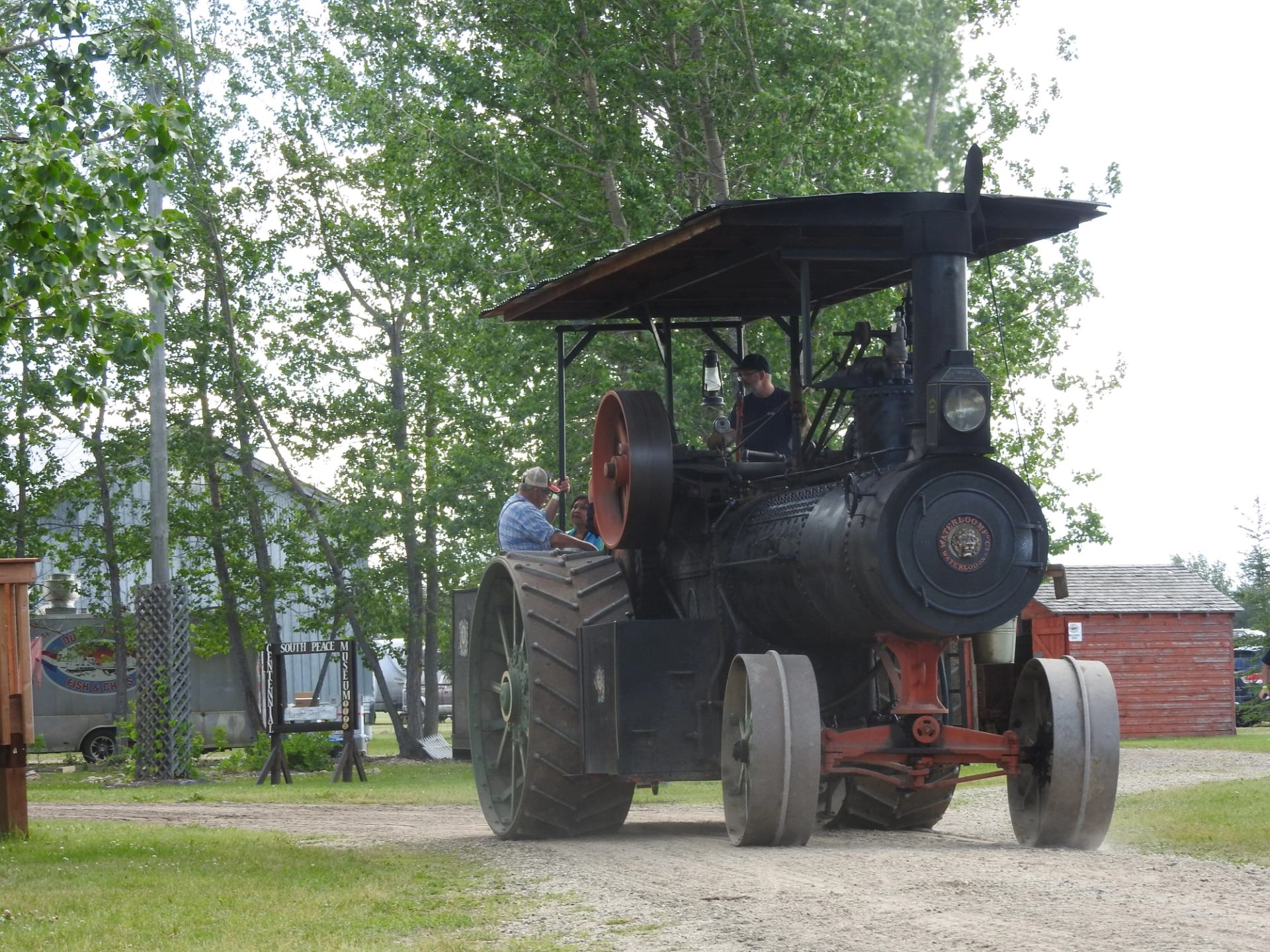 Steam locomotive with three people standing on the cab at South Peace Museum grounds.