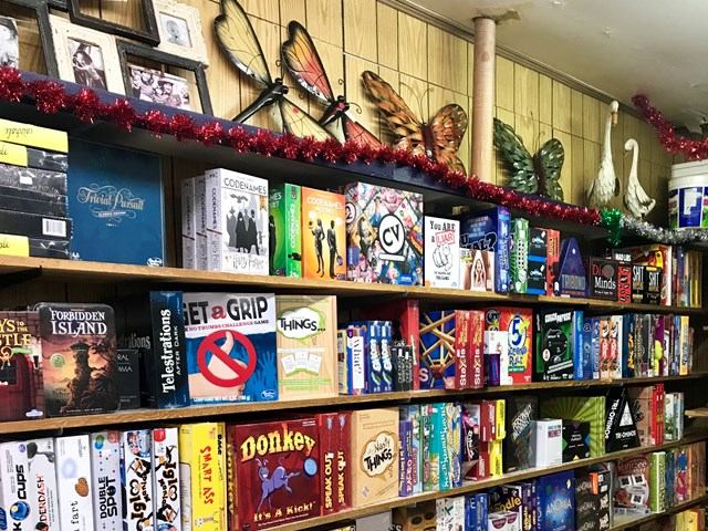 Books, gifts and colourful board games on shelves inside a shop with butterfly wall decor.