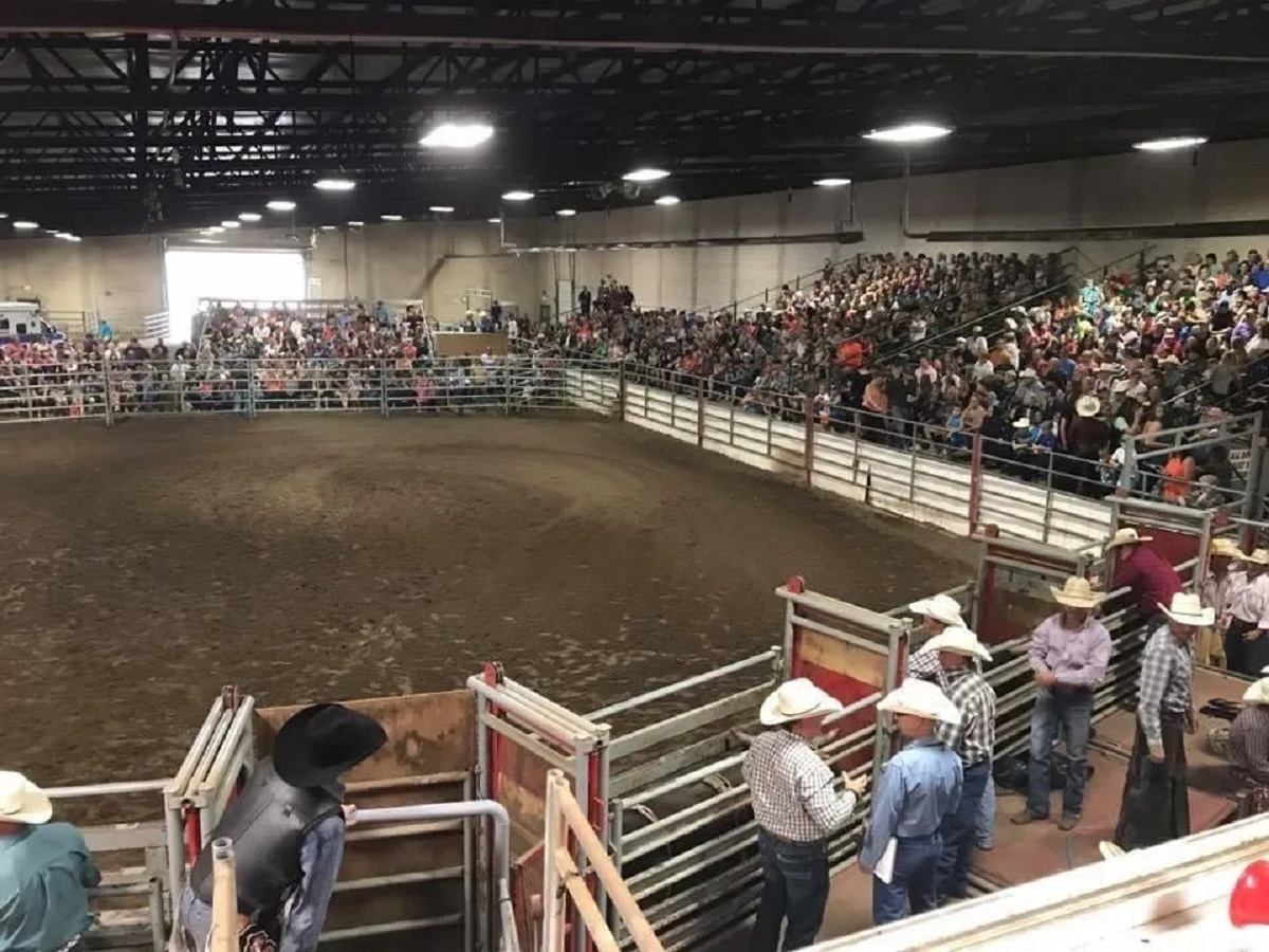 Indoor rodeo arena with a full crowd and riders preparing near the chutes.