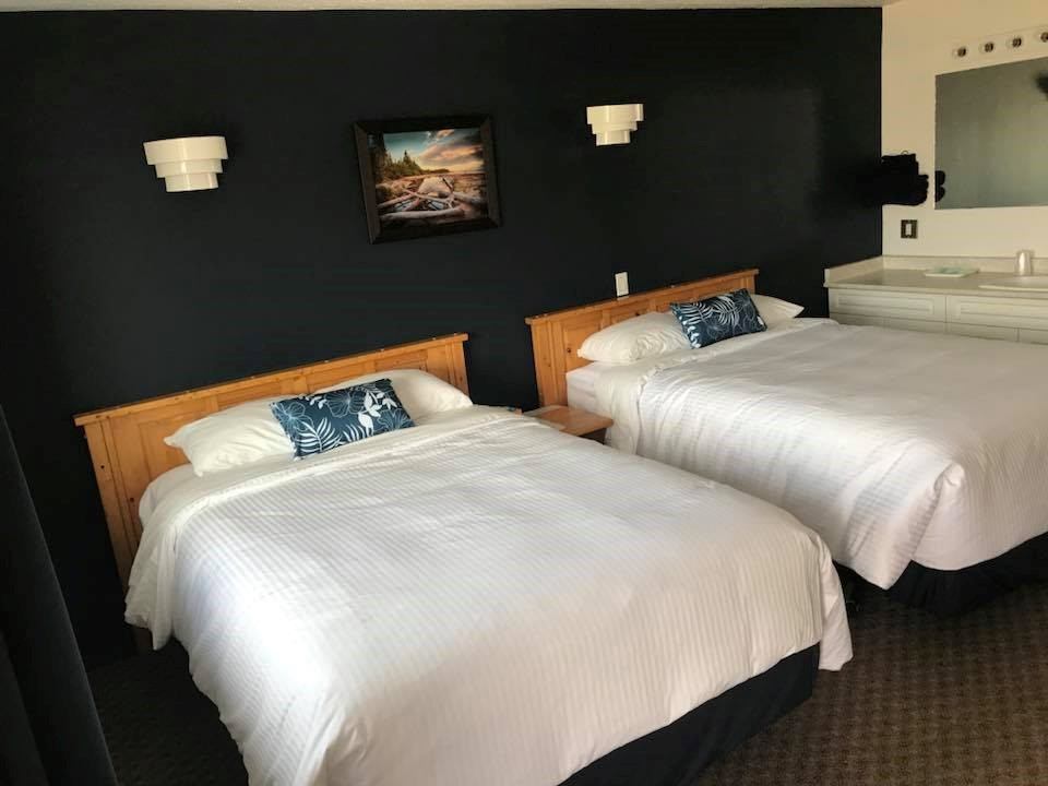 Hotel room with two neatly made beds, dark accent wall, and bedside lamps at Nordegg Lodge.