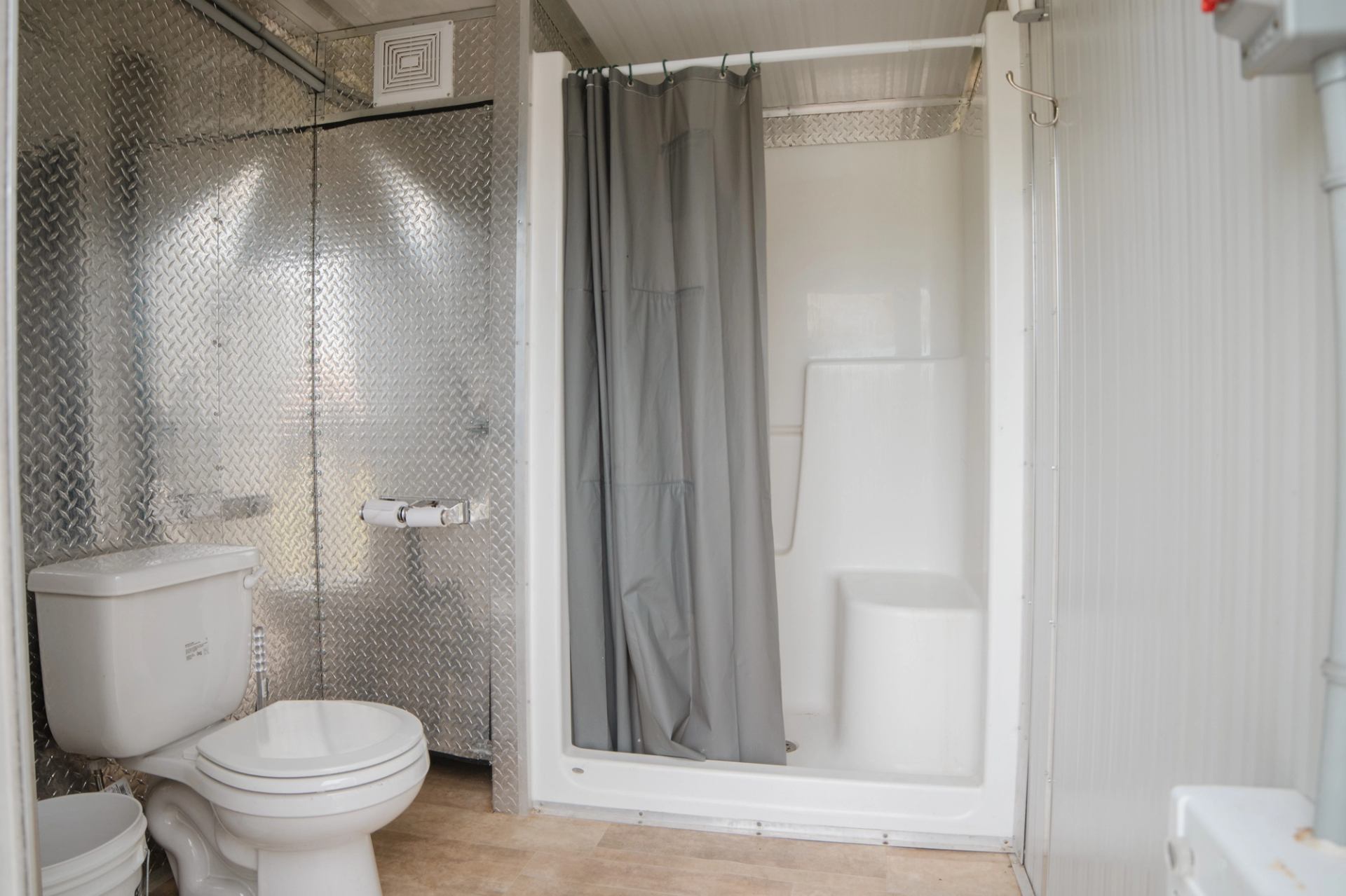 Compact bathroom with white toilet, metal wall panels and shower stall with grey curtain.