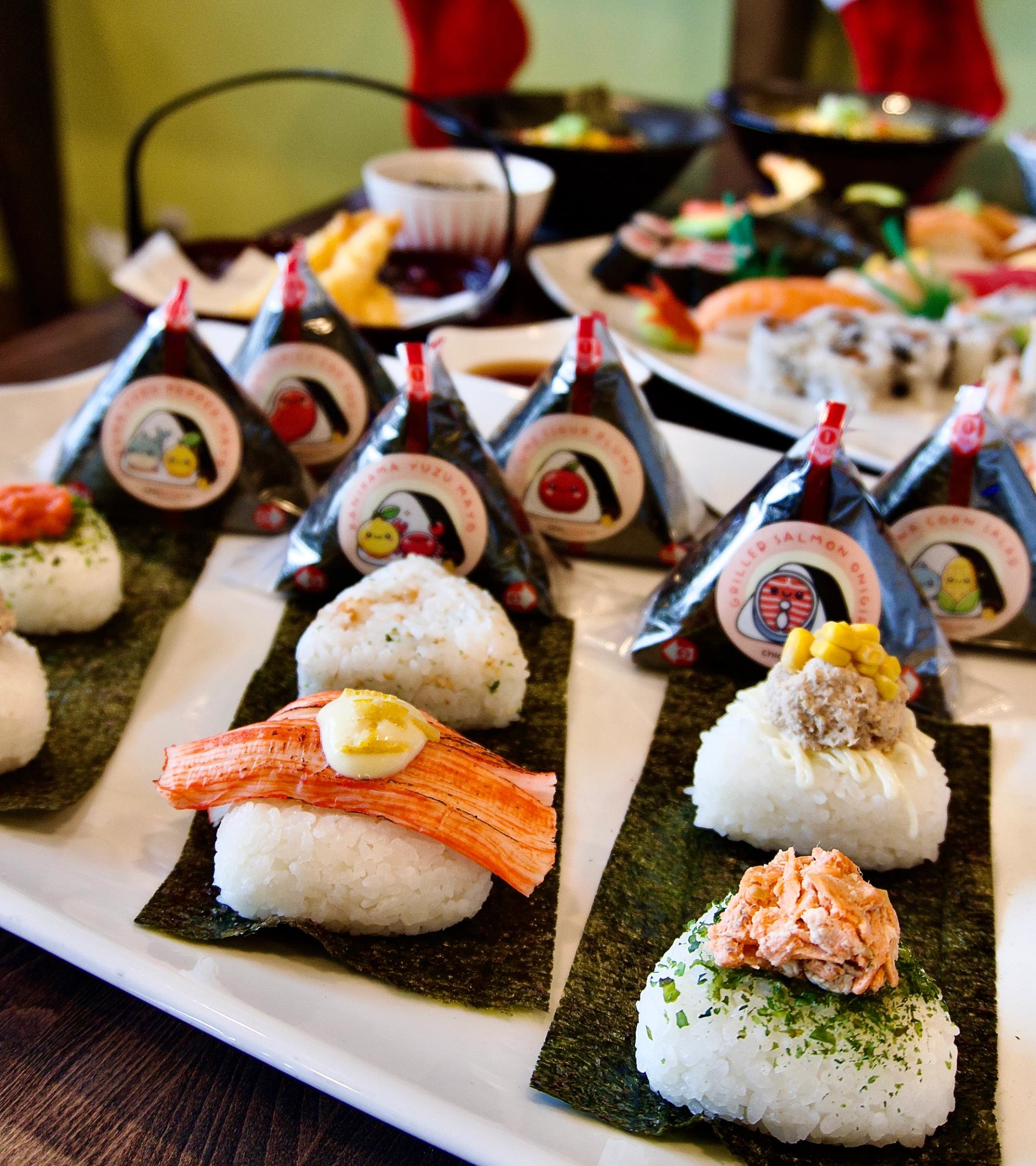Rice balls with seafood toppings and wrapped seaweed triangles arranged on platters.