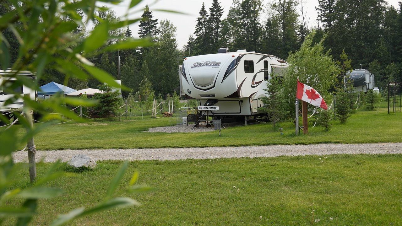 Large RV parked on a grassy campsite with a Canadian flag and trees in the background.
