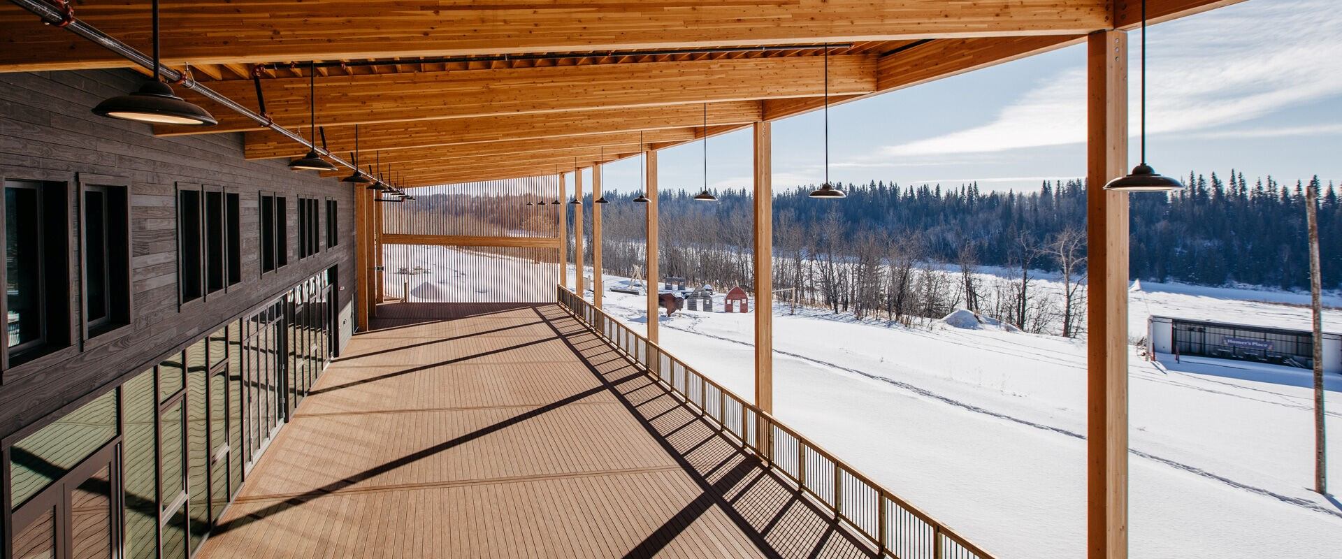 Deck at The Lodge, snowy ground below, forest in distance—Métis Crossing winter scene.