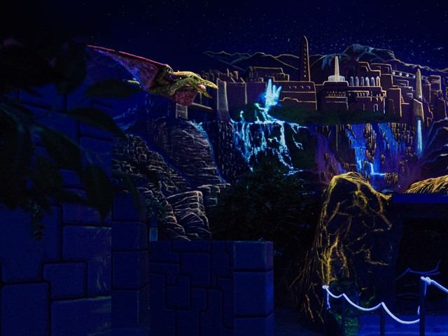Neon-lit exhibit with pterosaur model flying over cliffs and a glowing waterfall.