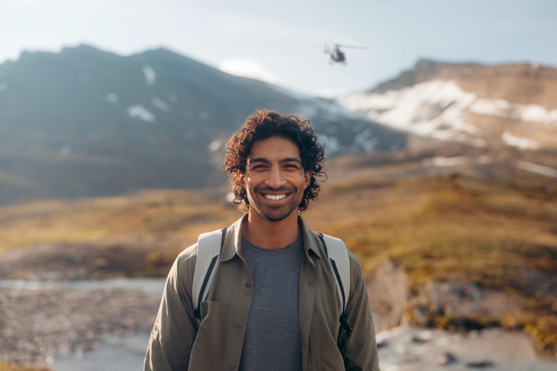 Person standing in a scenic mountain valley with a helicopter flying overhead.