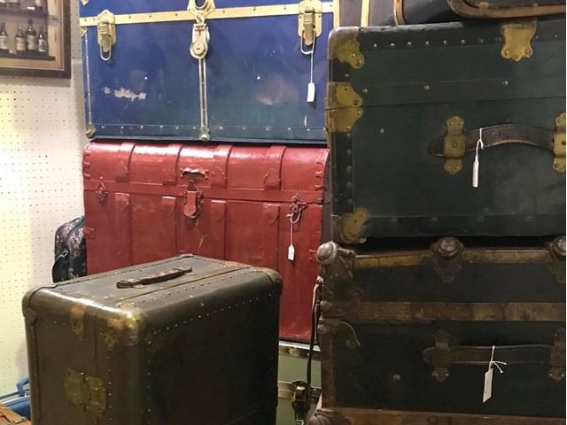 Stack of vintage travel trunks with price tags in an antique shop.