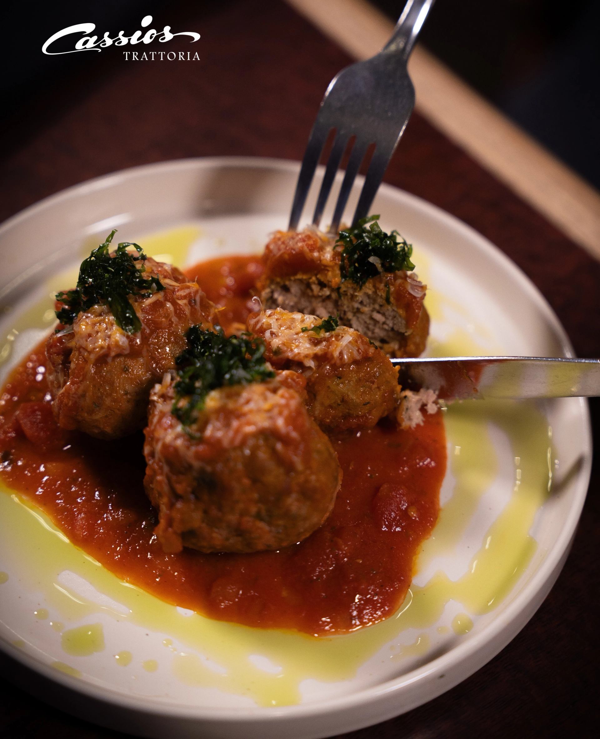 Plate of meatballs in tomato sauce with herbs, fork and knife cutting one.