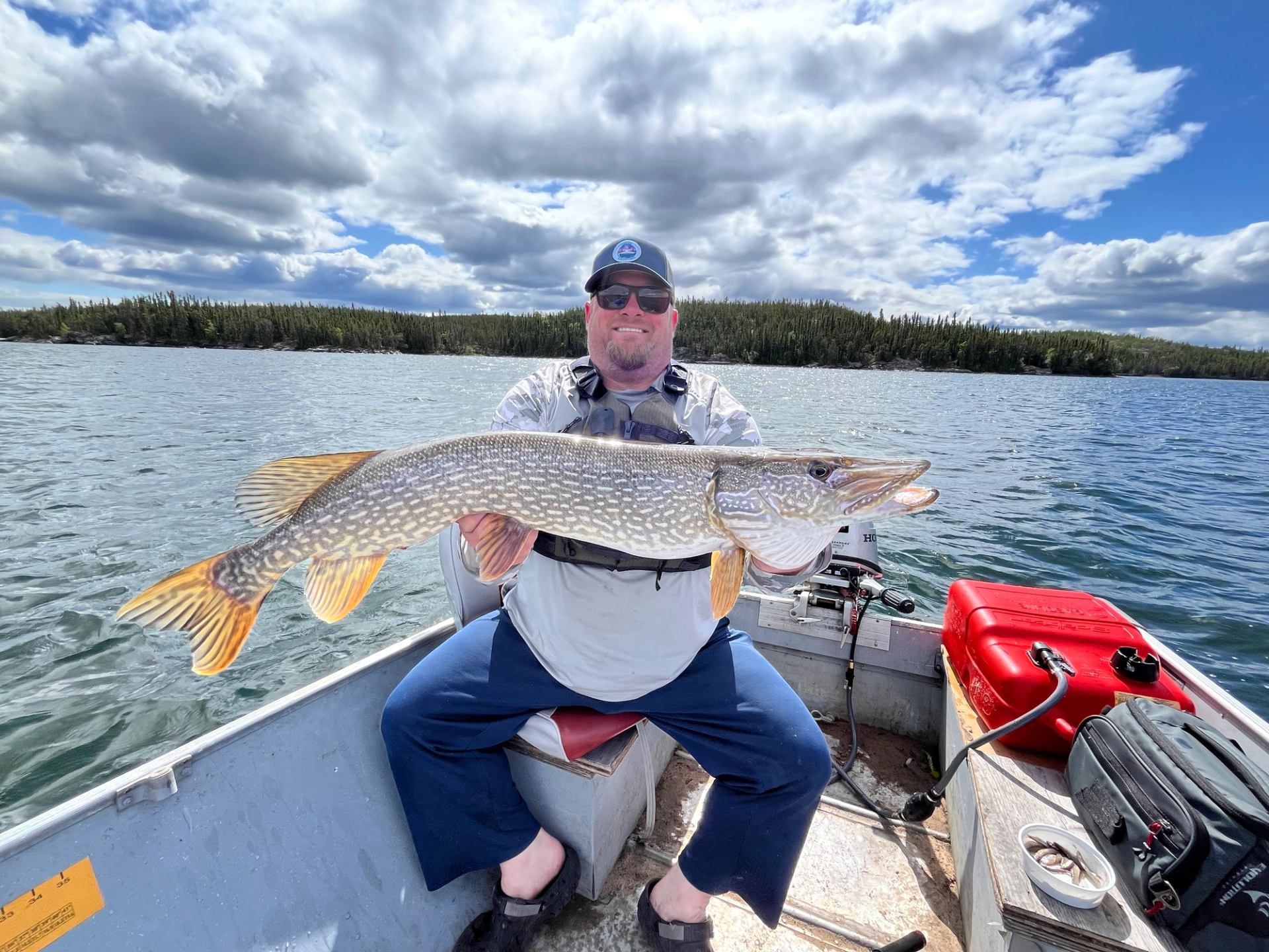 Person in boat holding large fish on calm lake with forested shoreline.