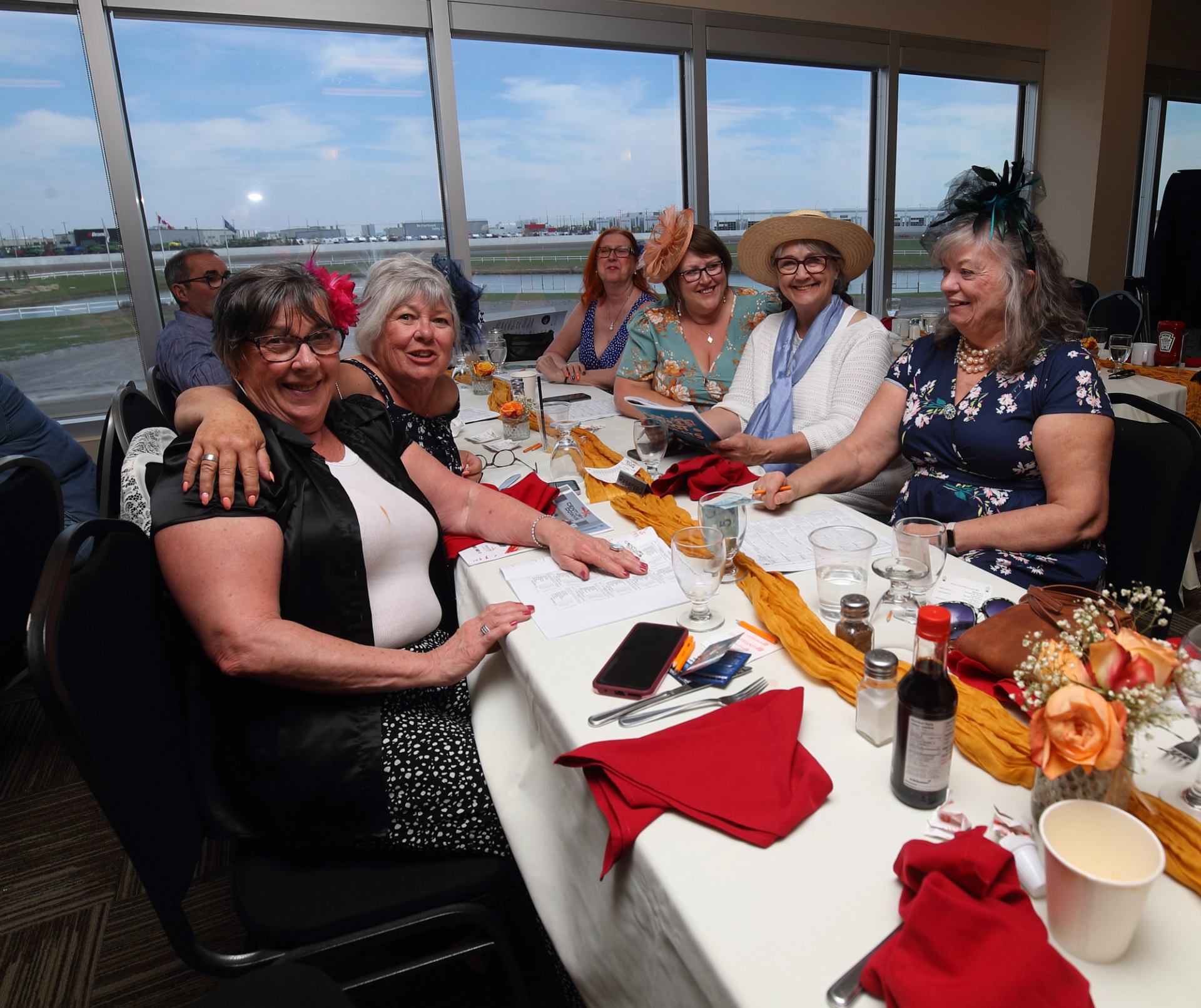 Group seated at a decorated table enjoying brunch near large windows overlooking a racetrack.