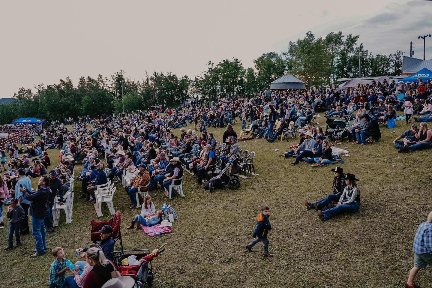 Large crowd seated on a grassy hillside overlooking the rodeo grounds at the Daines Ranch Pro Rodeo.
