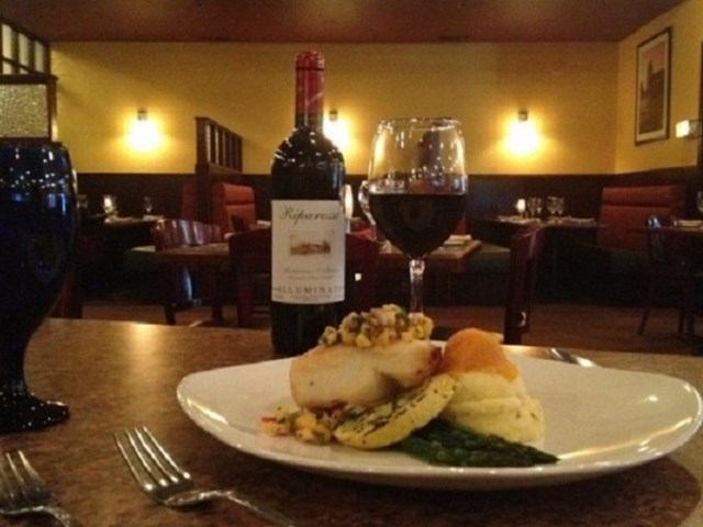 A plate of food, a bottle of red wine, and a glass of red wine on a table in a restaurant.