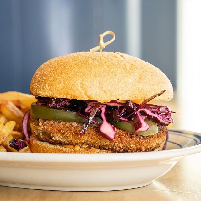 Fried meat sandwich with pickles and cabbage, served with fries on a plate.