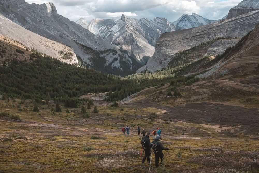 Hikers walking through a green valley with towering mountains in the background.