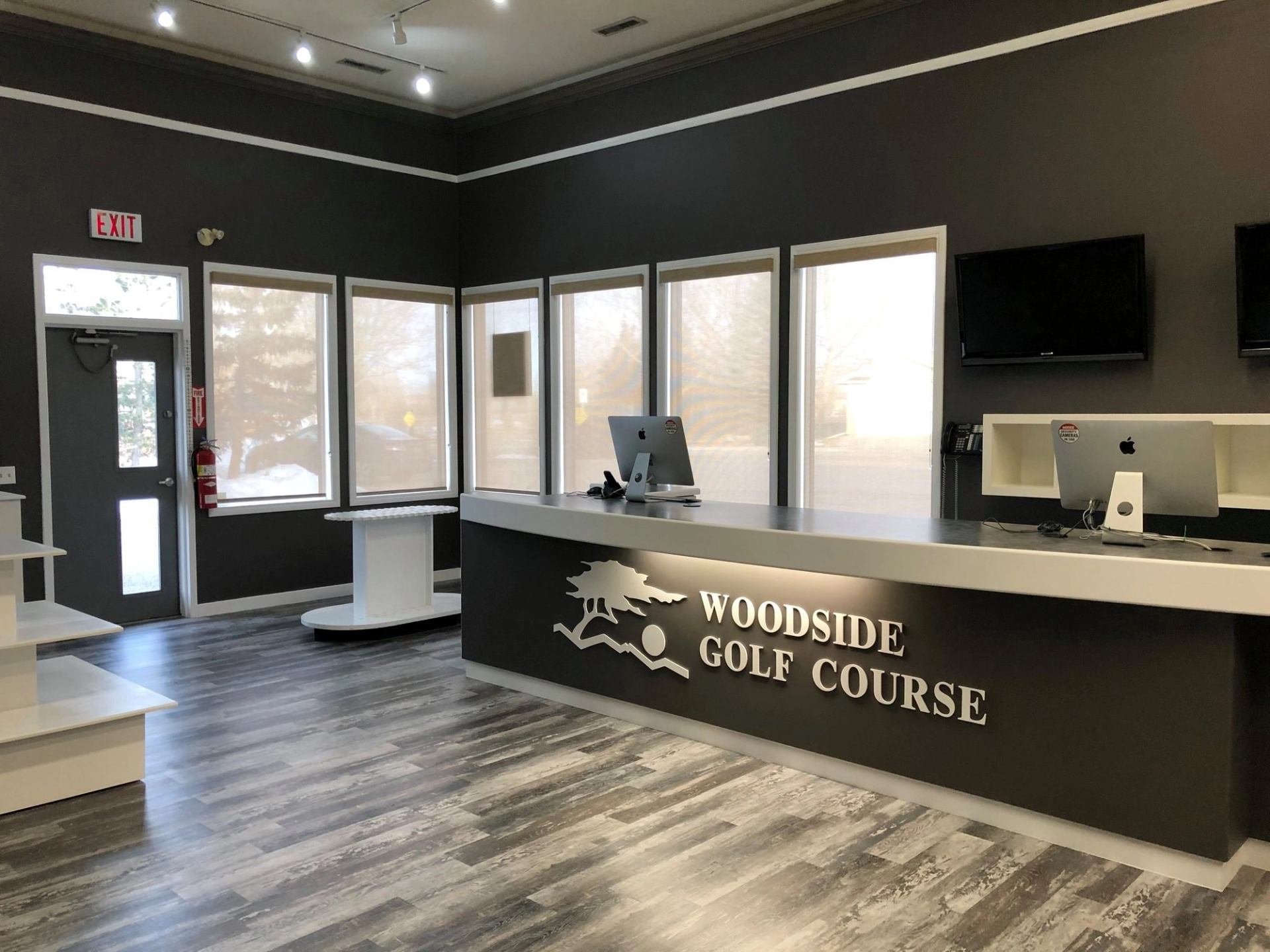 Modern reception desk at Woodside Golf Course with sleek gray design and logo.