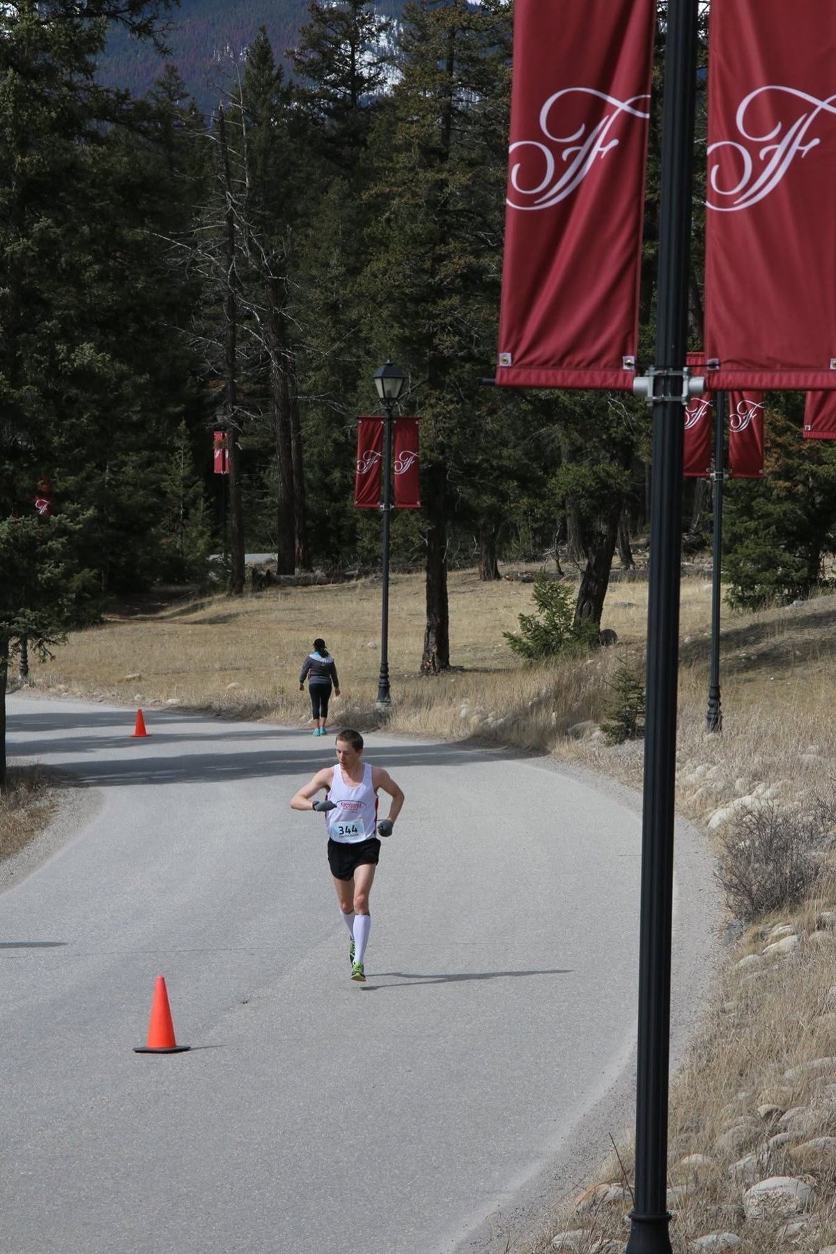 Runner in race bib passes orange cone on paved path lined with red banners.