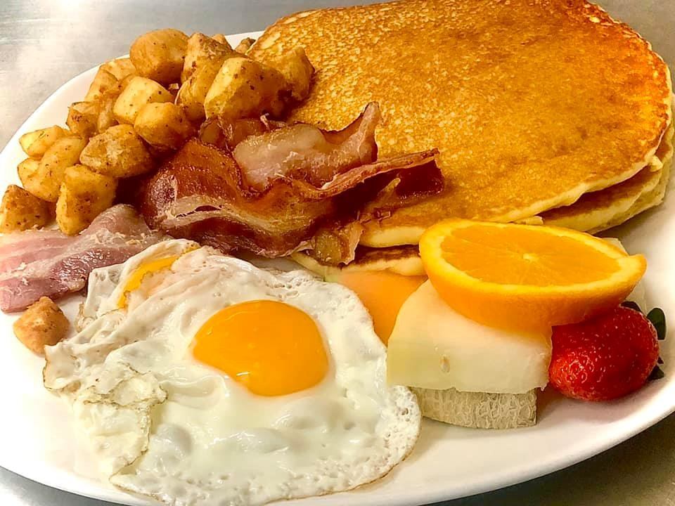 Breakfast plate with eggs, bacon, home fries, pancakes, and fruit.