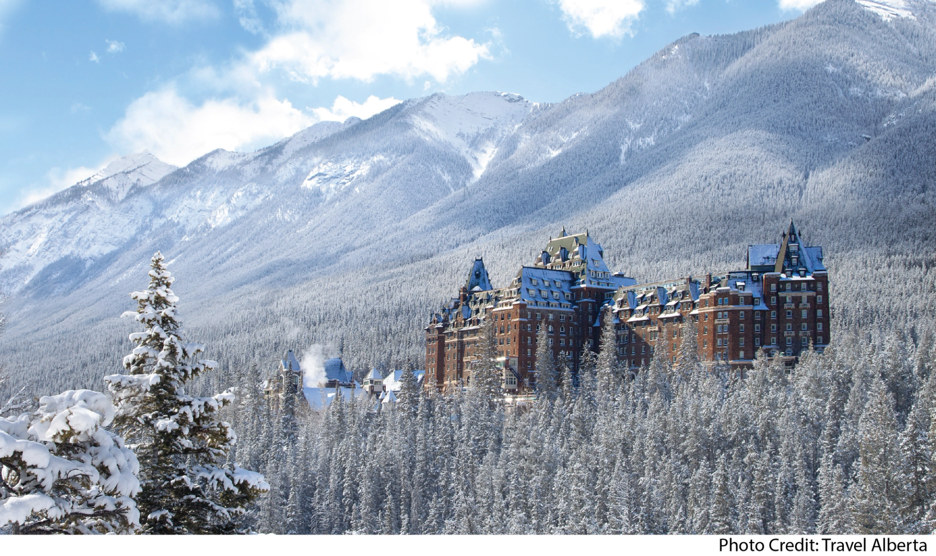 Historic Fairmont Banff Springs hotel surrounded by snow-covered trees and mountains.