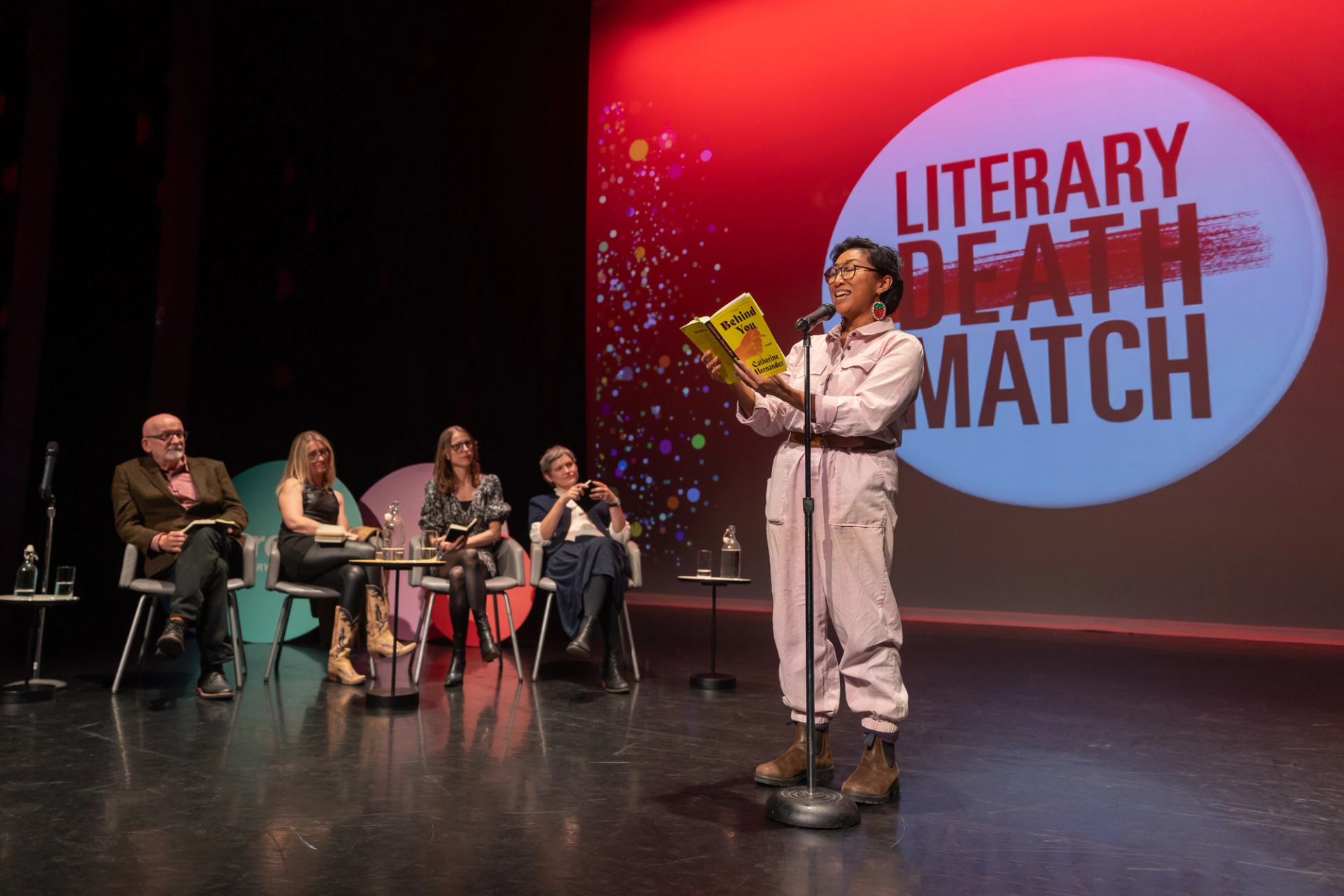 Reader holds a book at a microphone during Literary Death Match.