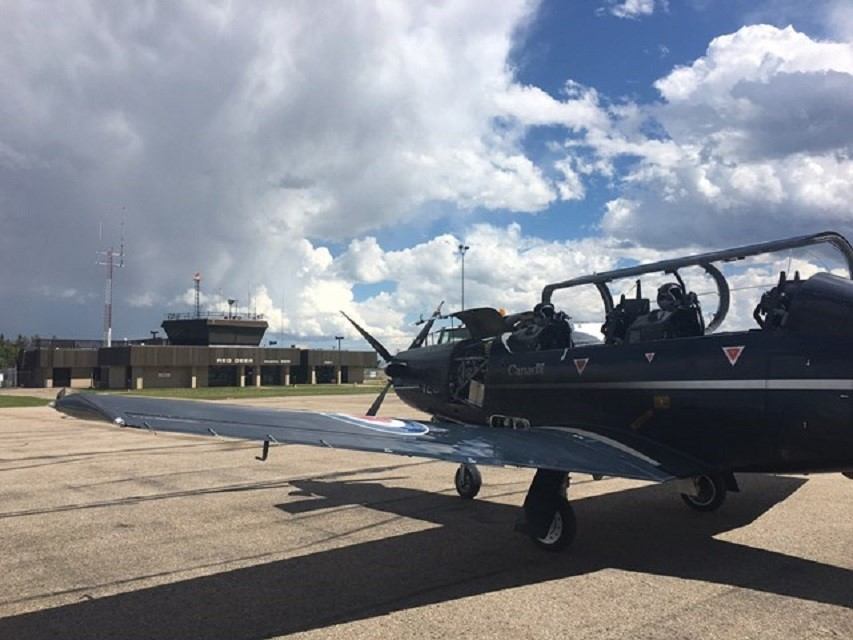 Dark aircraft parked on runway at Red Deer Airport, cloudy sky and distant buildings in background.