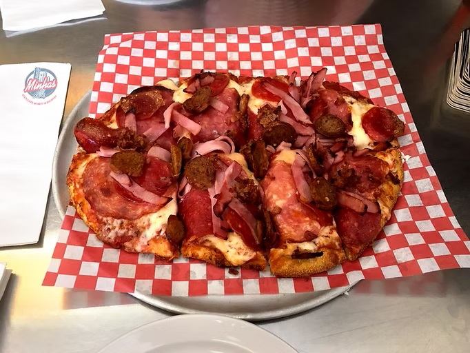 A specialty pizza topped with pepperoni, ham, sausage, and melted cheese sits on a serving tray.