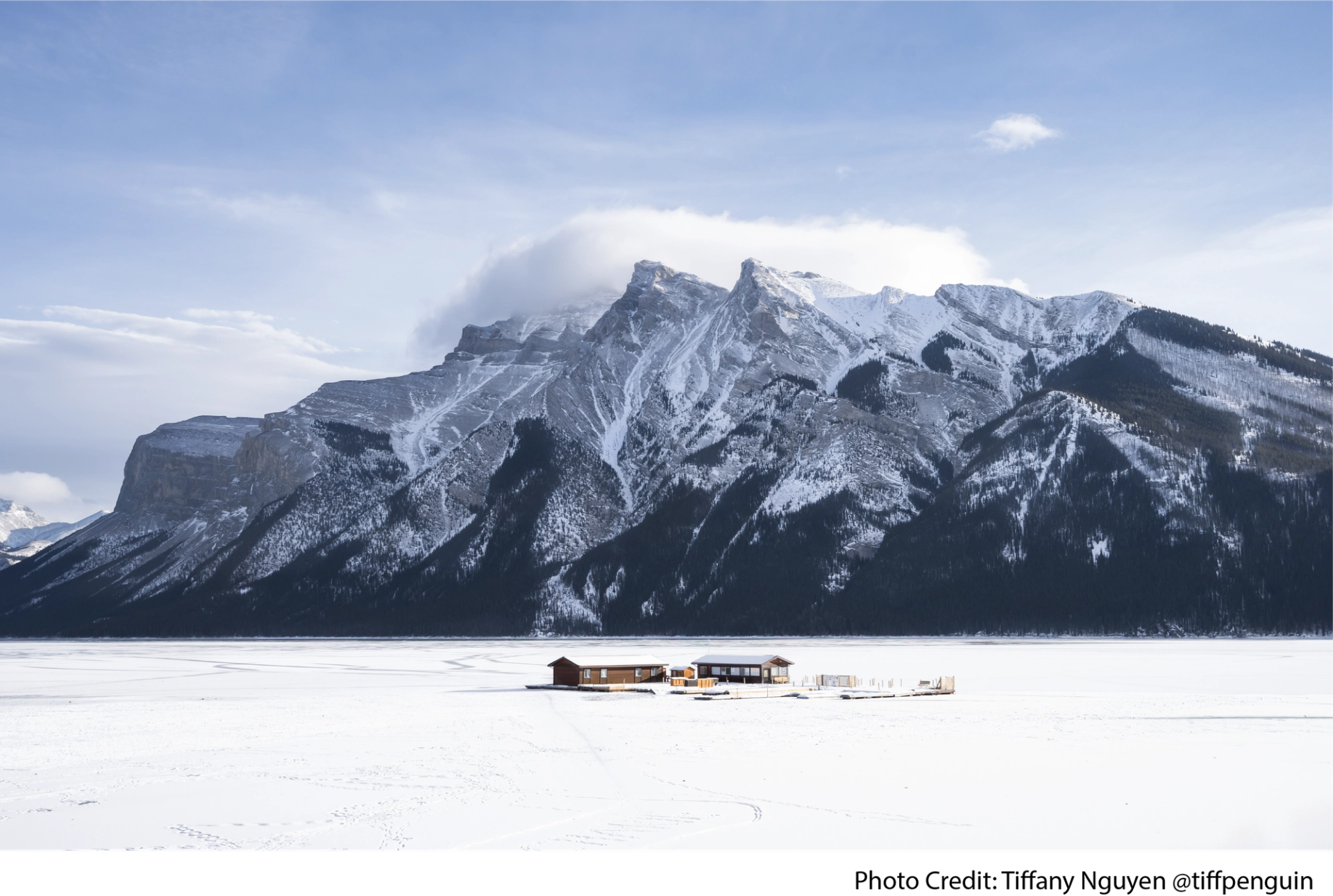 Snow-covered Lake Minnewanka with rugged mountains and a small dock in the distance.