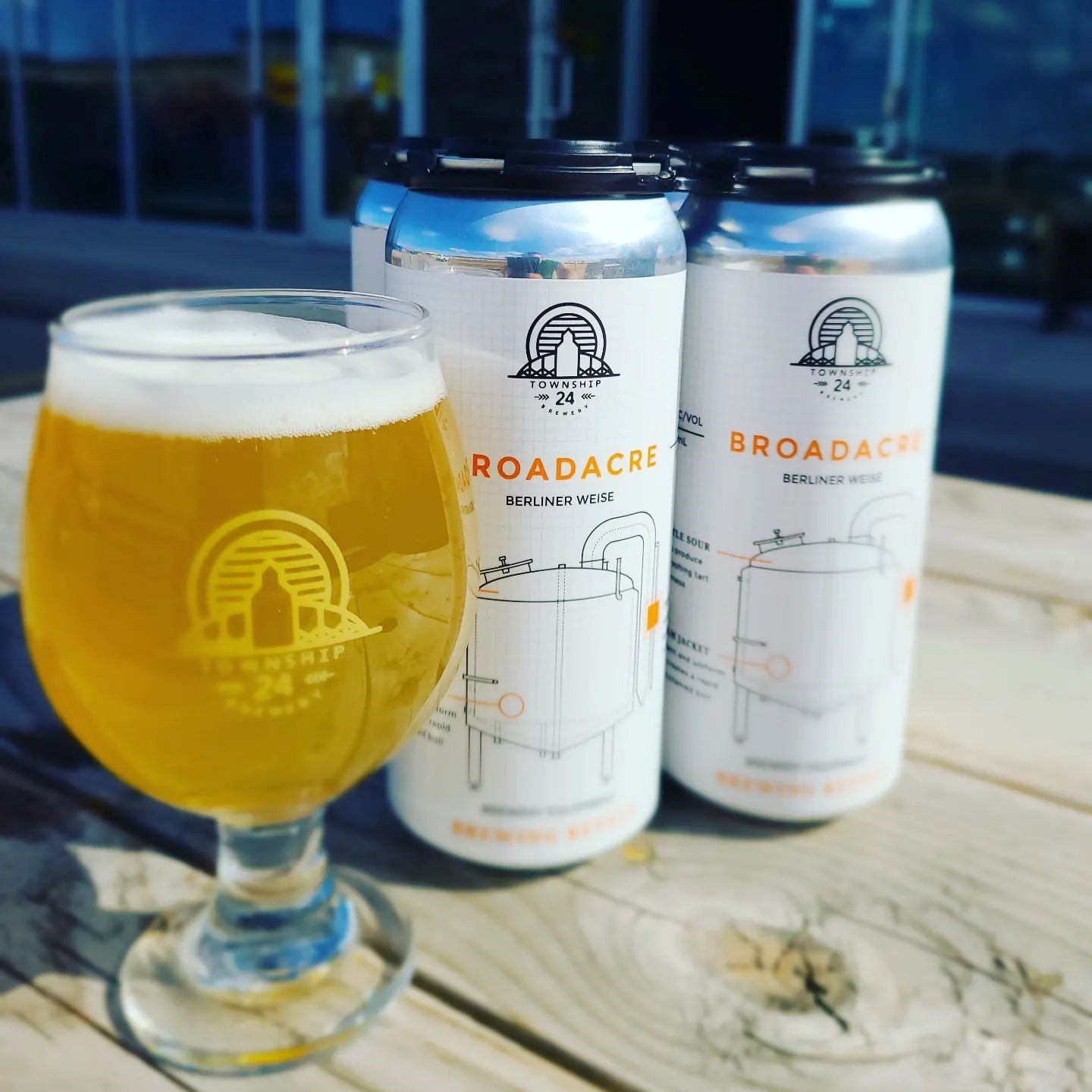 Beer glass and Township 24 Brewery cans on a table, with “Broadacre” labels visible.