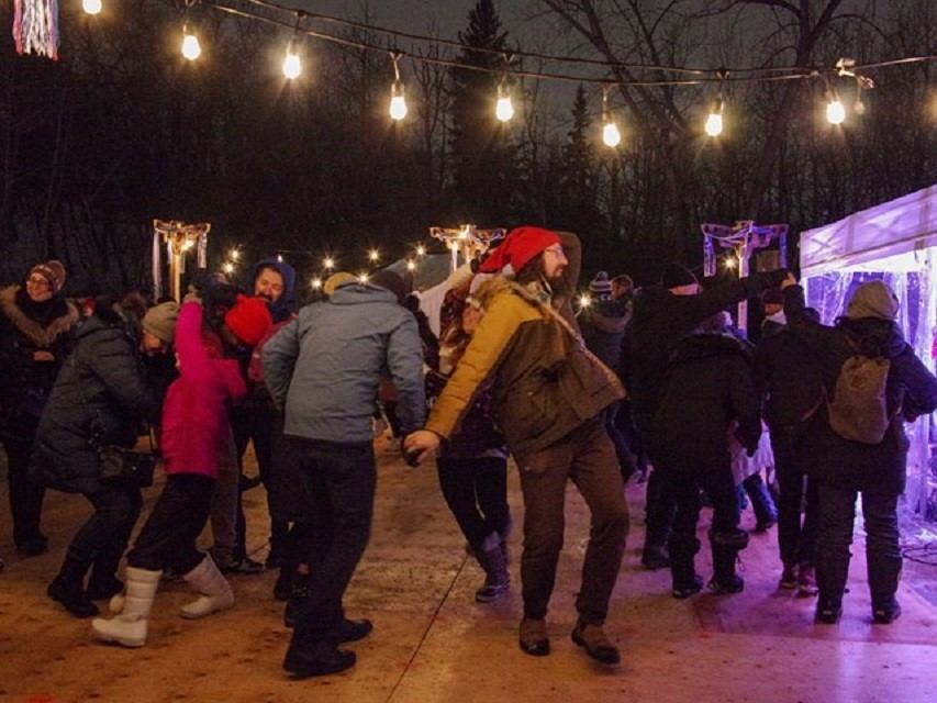 People in winter gear gather under string lights at night during outdoor festival.