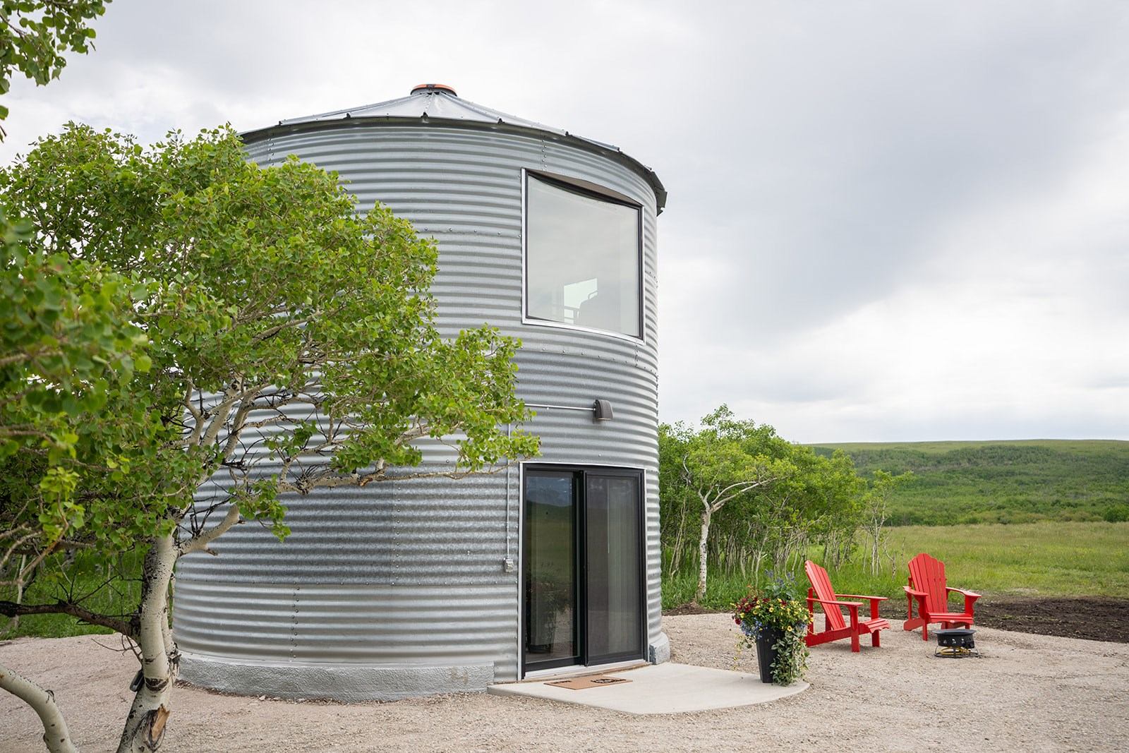 Two red Adirondack chairs outside a cabin made from a gain silo.