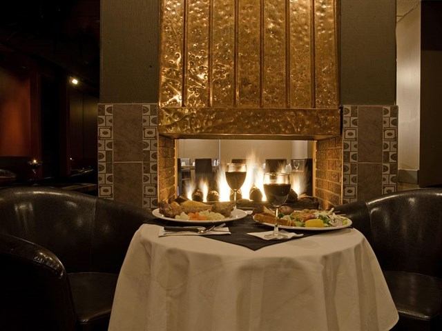 Cozy dining table for two set in front of a lit fireplace with plated meals.