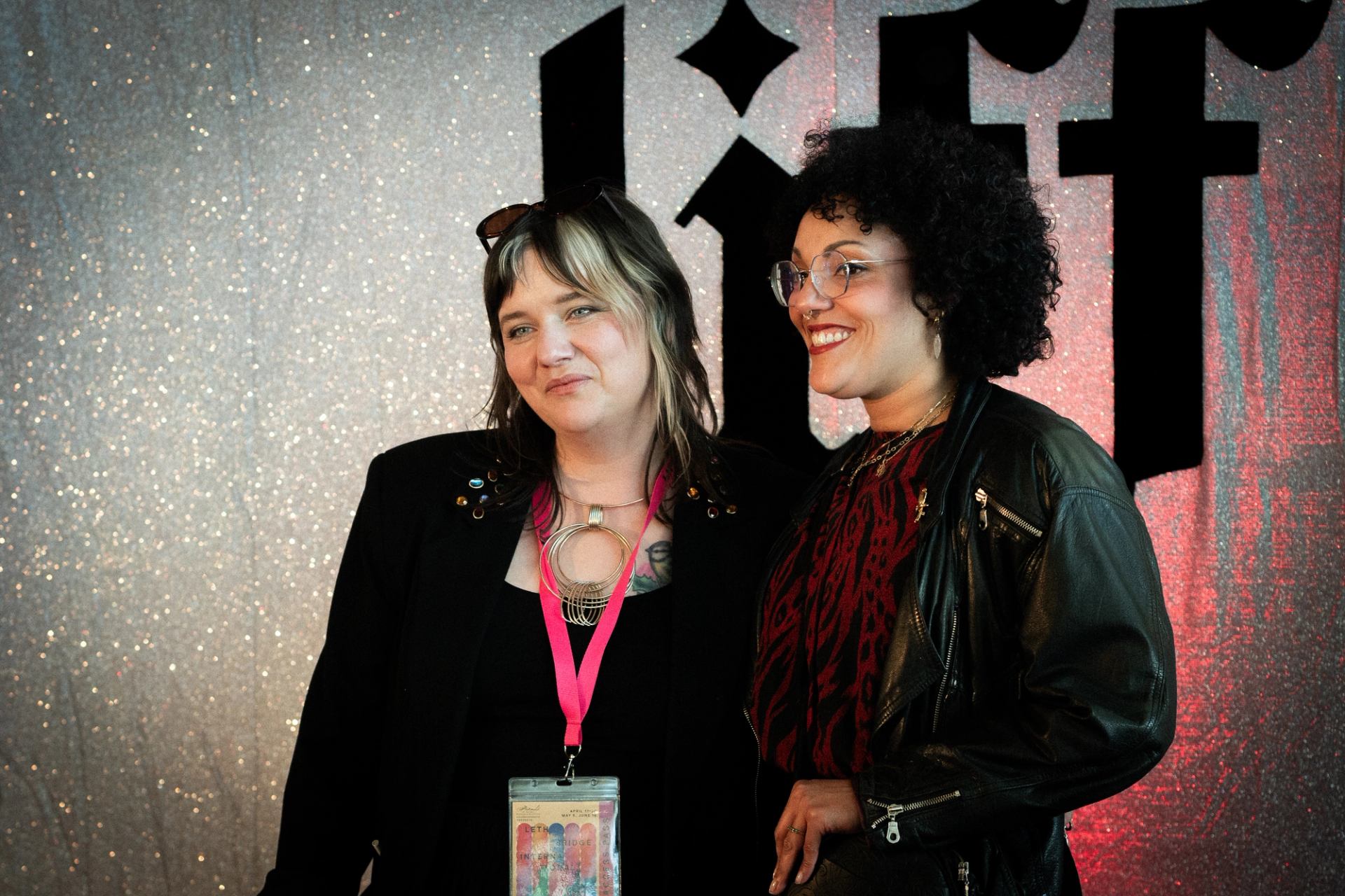 Two people stand together at an event, posing before a glittery backdrop.