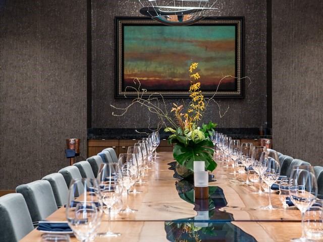 Table set with wine glasses and grey chairs in front of wall art.