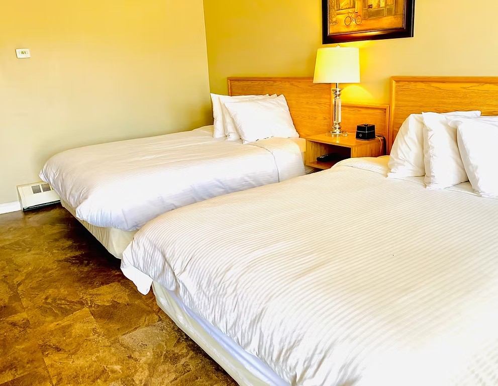 Guest room with two neatly made beds, bedside table, lamp, and neutral décor.