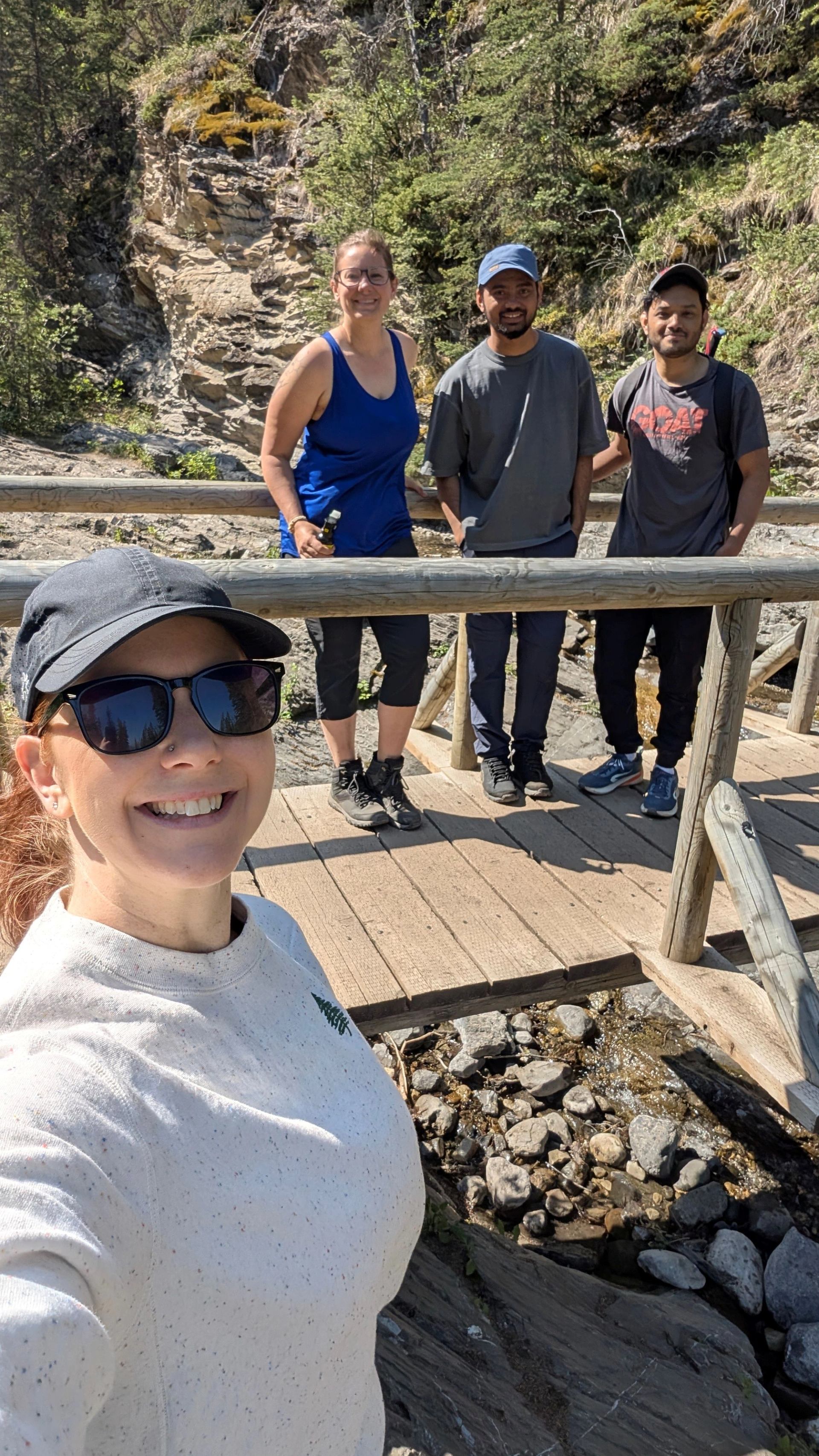 A group of people stood on a bridge while another person takes a selfie of them all.