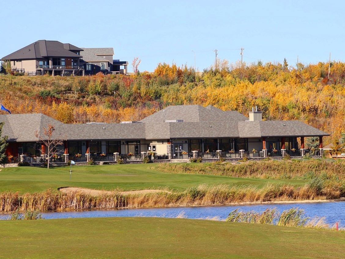 Clubhouse and autumn trees overlooking a golf green beside a water feature.