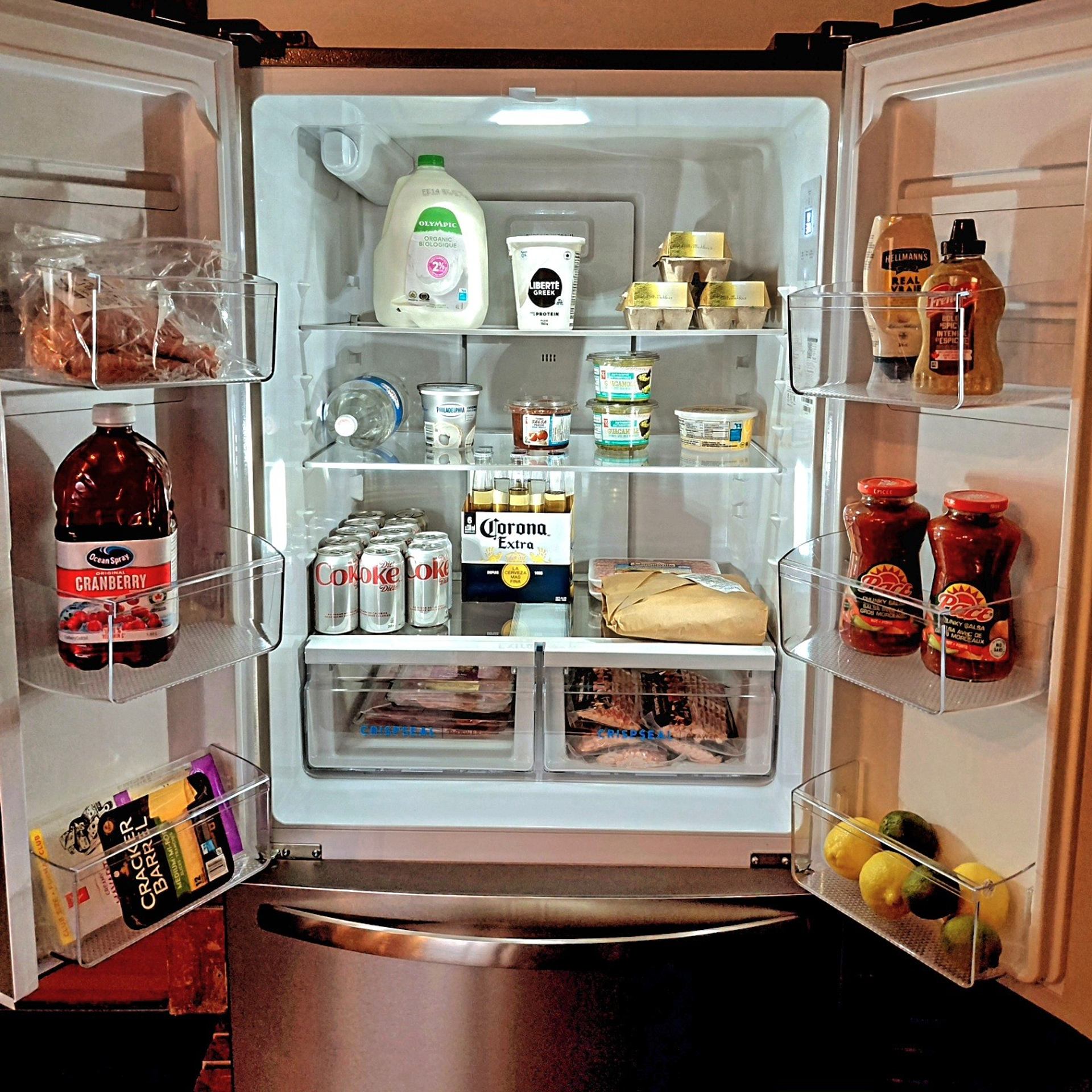 Open refrigerator with milk, soda, beer, condiments, packaged meat and fresh citrus.