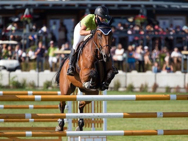Horse and rider jump over an obstacle at a show jumping event in an arena.