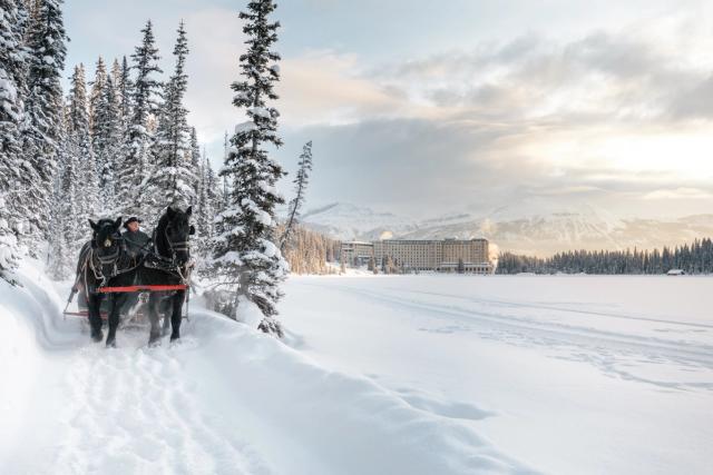 An early morning sleigh ride along a frozen Lake Louise with Fairmont Château Lake Louise in the background in Banff National Park.