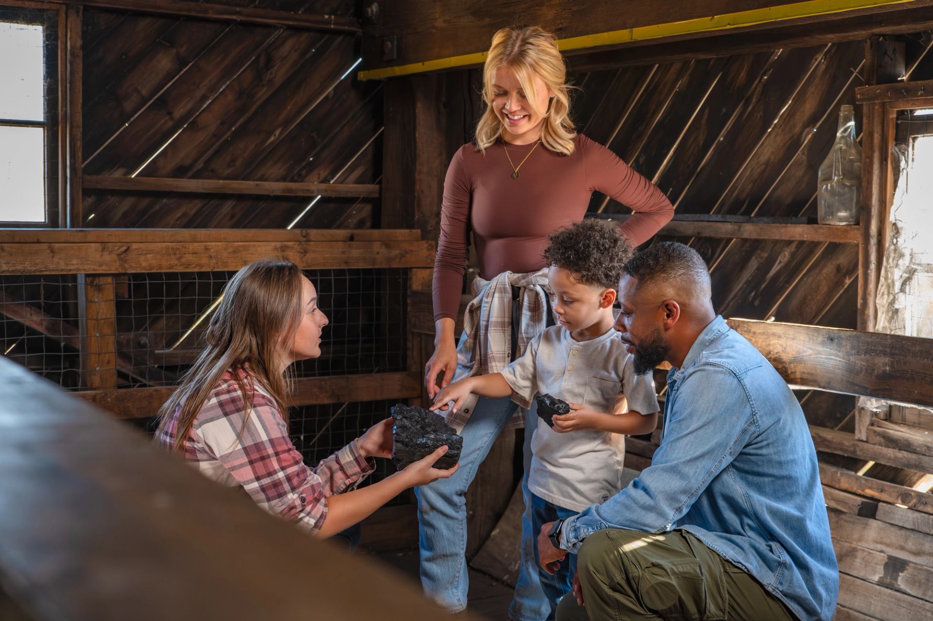 Group of people in wooden barn examining large black rocks together.