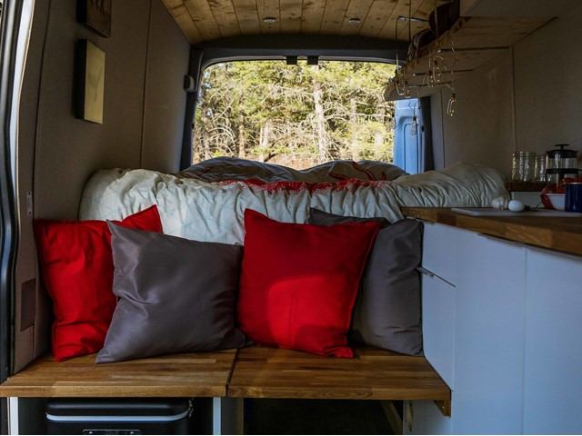 Stylish campervan interior with bed, cushions, and compact kitchen setup.