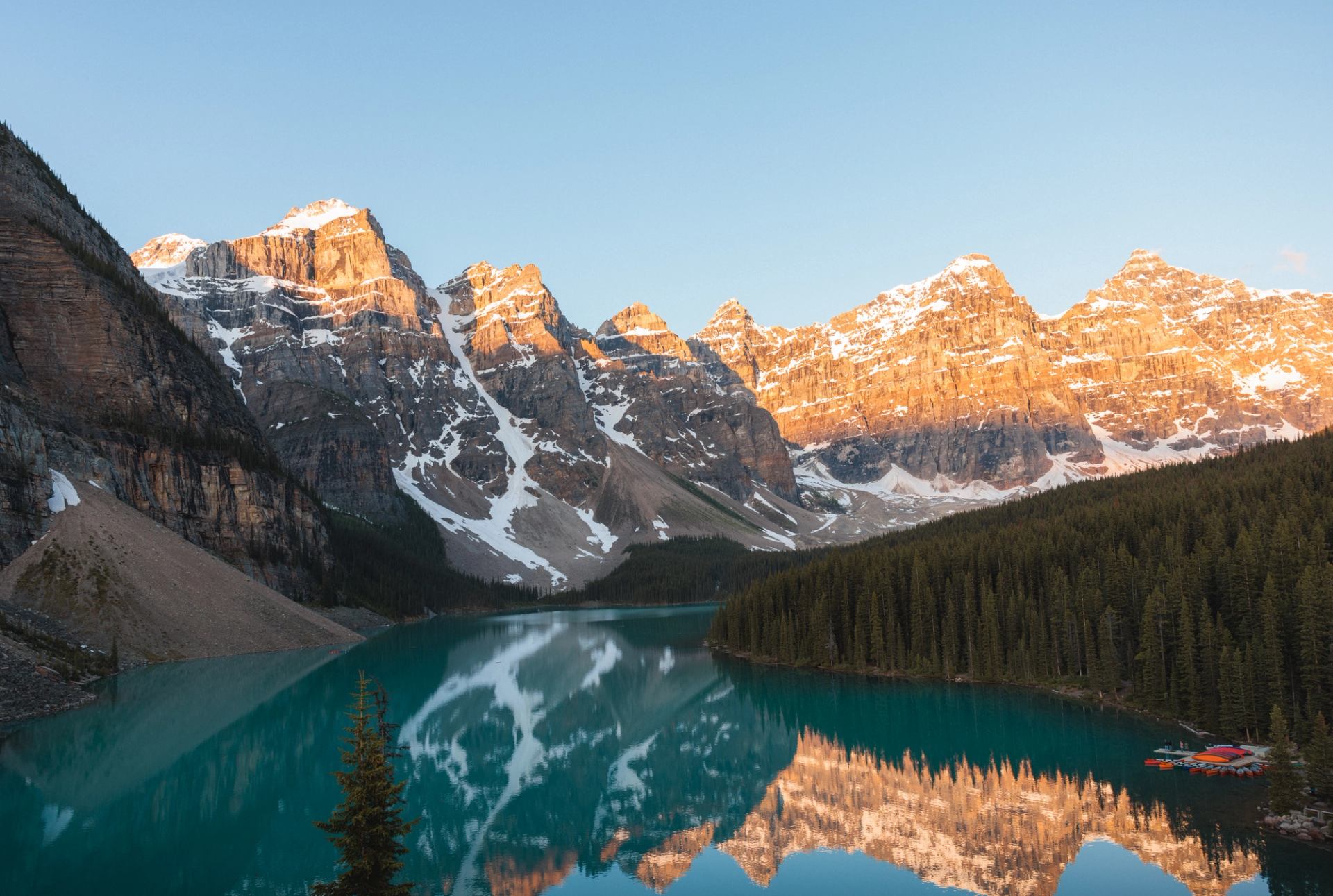 Turquoise mountain lake reflecting snow-capped peaks and dense evergreen forest at shoreline.