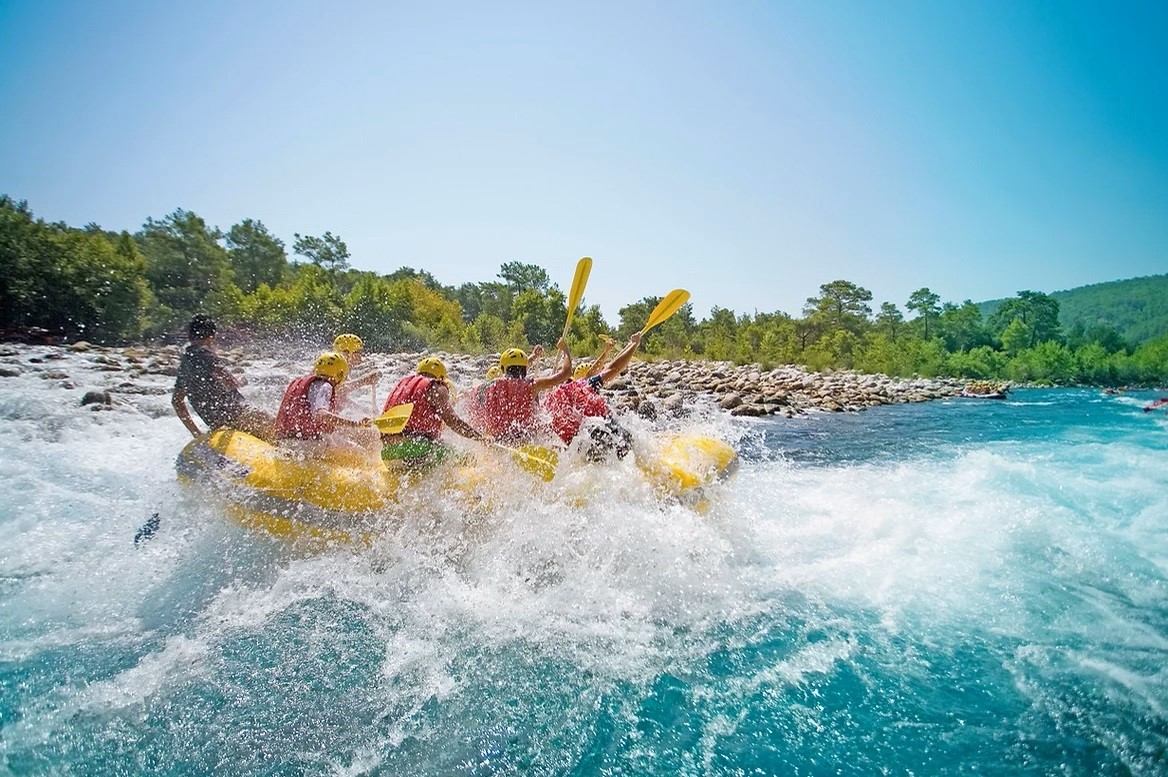 Group rafting on river with helmets and life jackets in scenic forest setting.