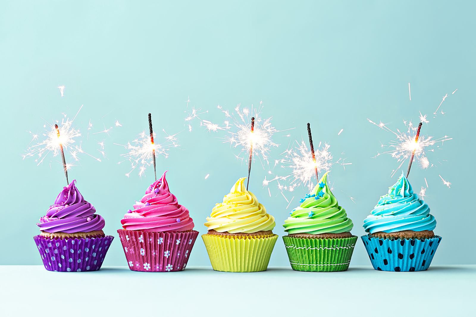 Colorful cupcakes with sparklers against a blue background.