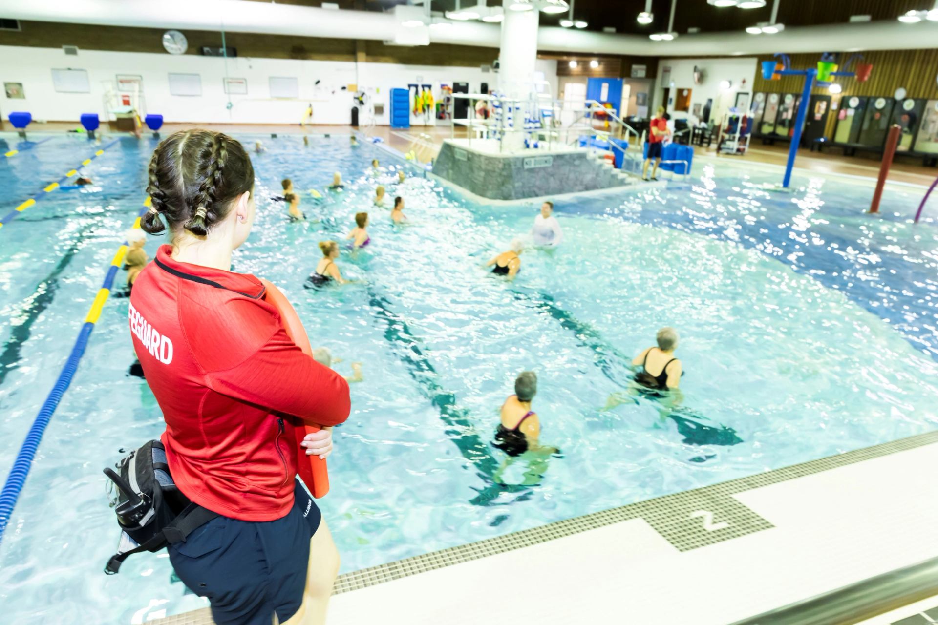 A lifeguard watches a group do shallow water fitness class.