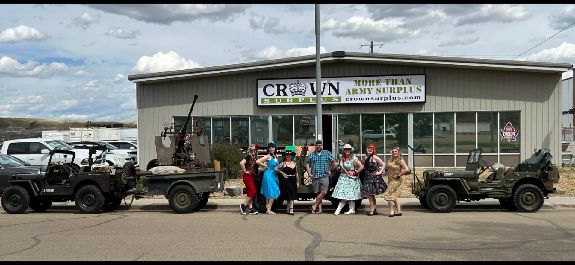 Crown Surplus Store exterior with people posing between military vehicles in front of storefront and signage.