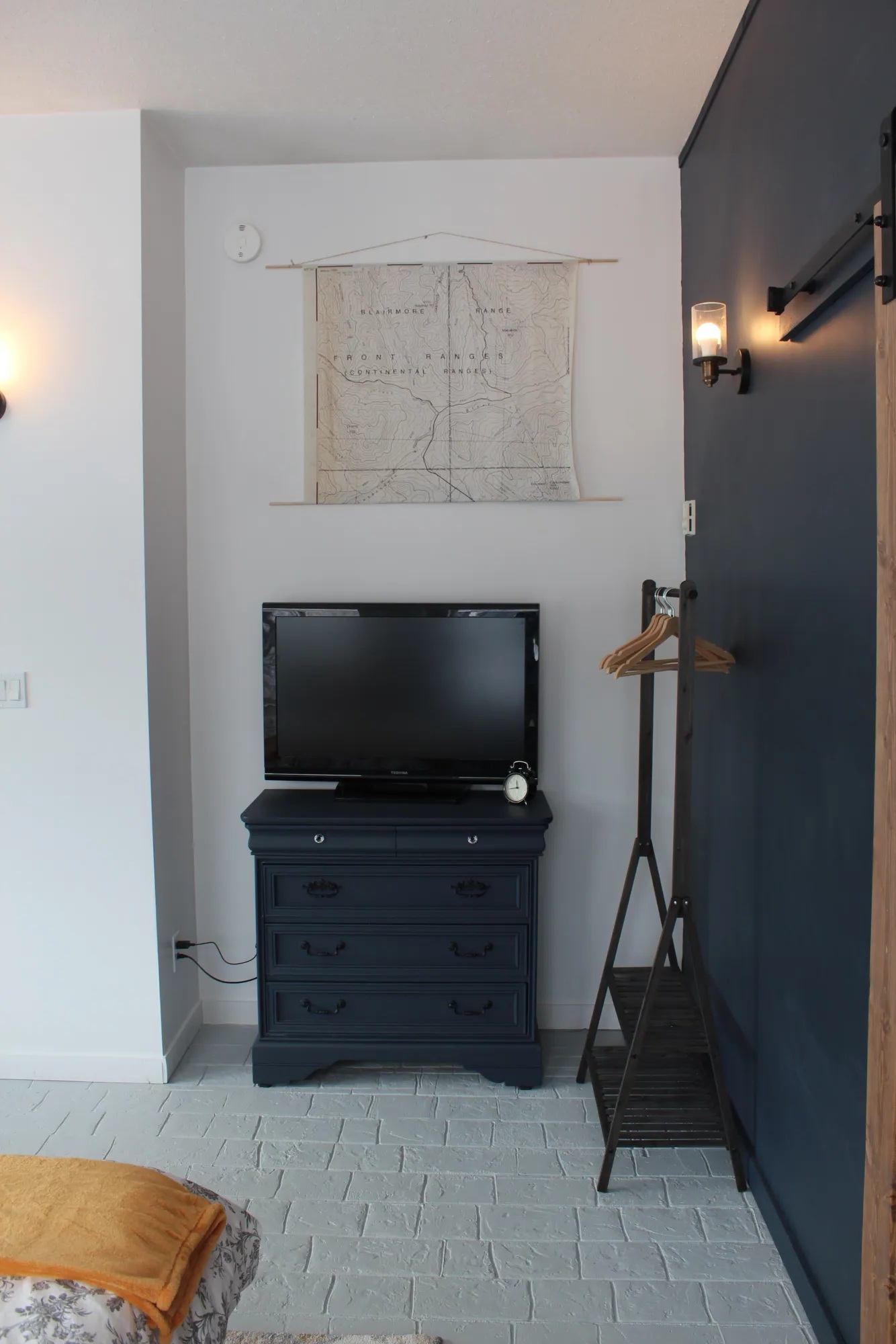 Bedroom corner with TV on navy dresser, wall map, and clothes rack with hangers.