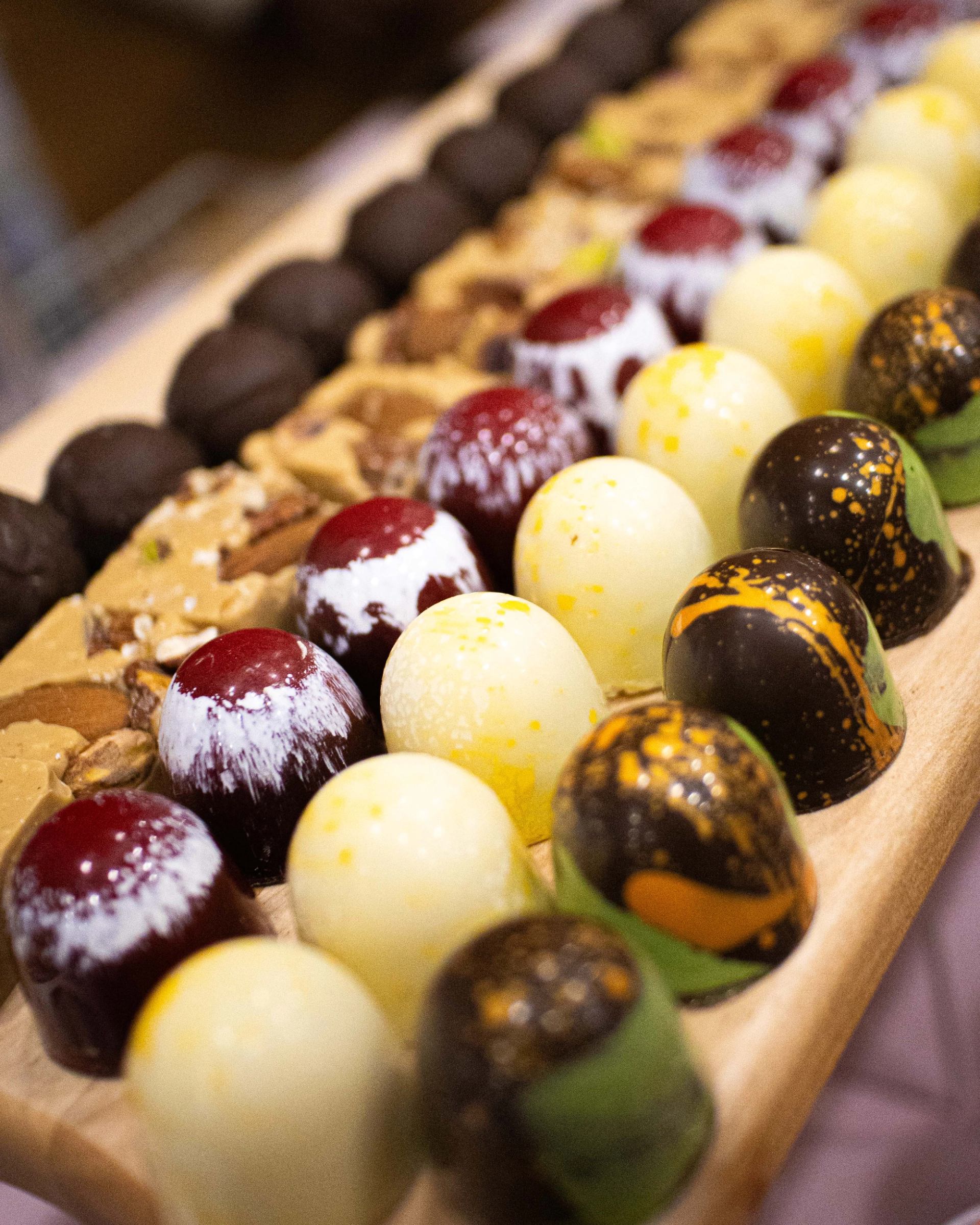 Assorted gourmet chocolates arranged in neat rows on a wooden serving tray.