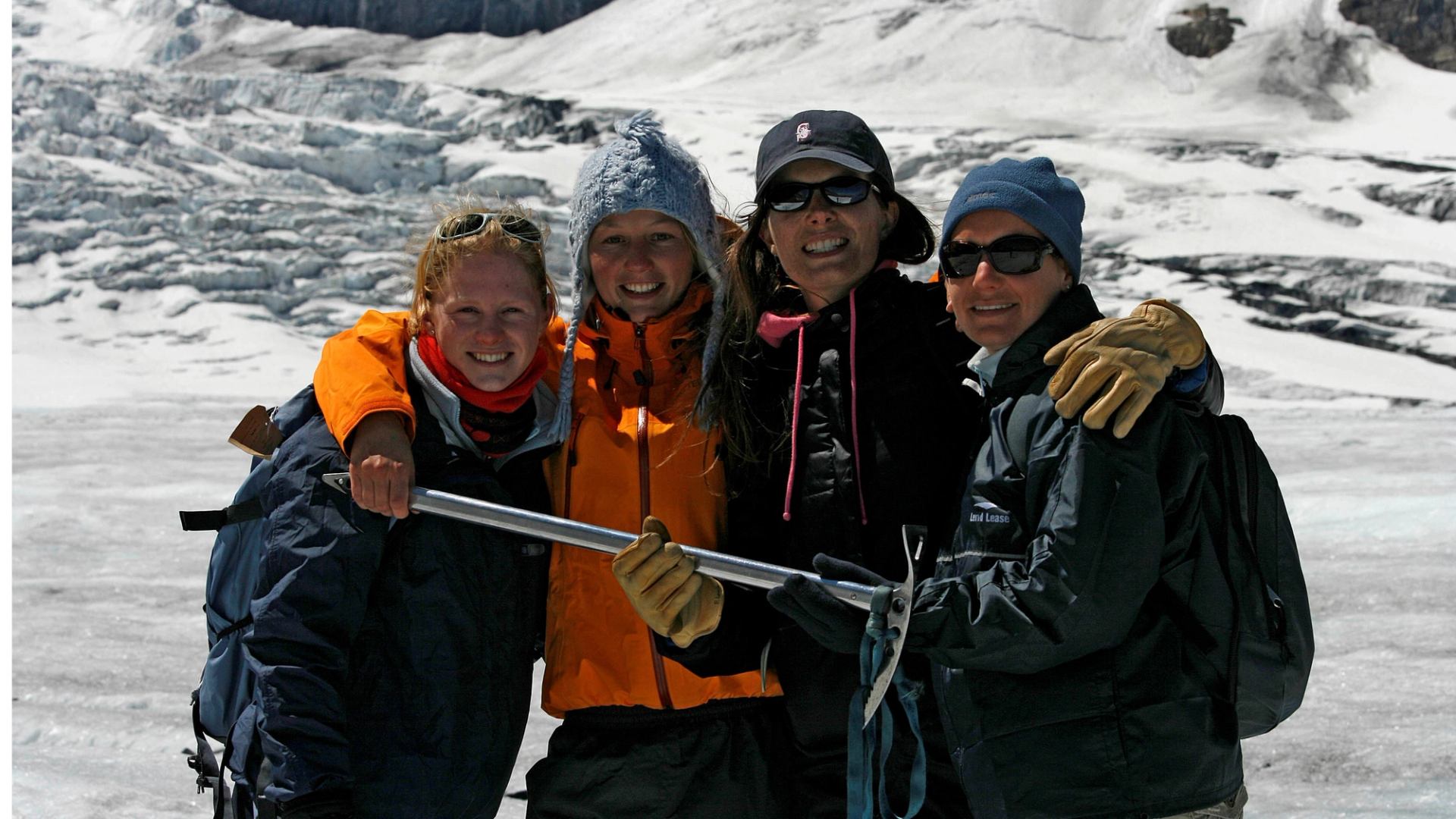 Group of hikers in winter gear holding an ice axe on a glacier.