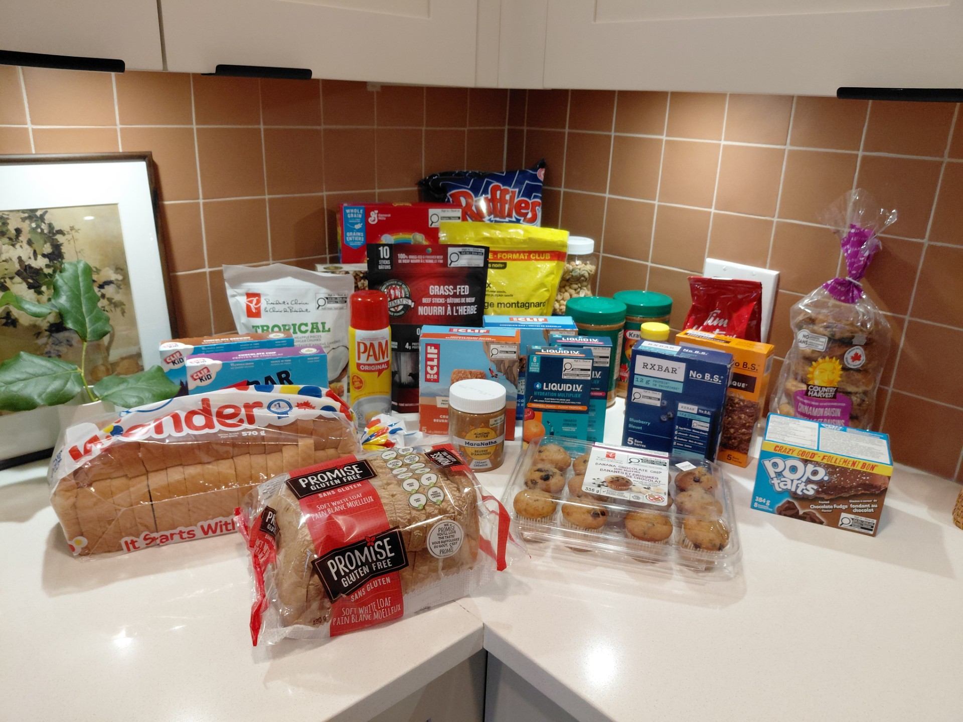 Packaged breads, snacks, drinks and baking supplies cover a kitchen counter.